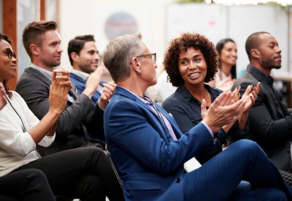 Group Of Businessmen And Businesswomen Applauding Presentation At Conference