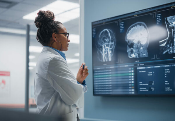 Medical Science Hospital: Confident Black Female Neurologist, Neuroscientist, Neurosurgeon, Looks at TV Screen with MRI Scan with Brain Images, Thinks about Sick Patient Treatment Method. Saving Lives
